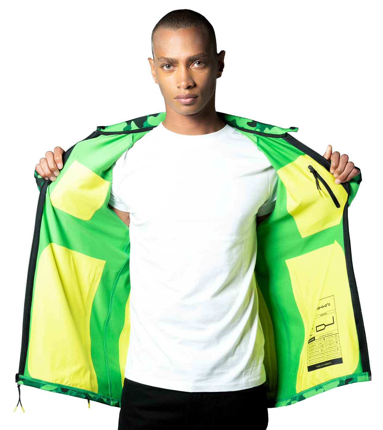 A person in a white shirt holds open the GREEN-CAMO CASUAL JACKET by Machina - Wearable Technology to display its interior. Made with sustainable fabrics, this smart casual jacket features multiple pockets and boasts a geometric pattern on the exterior. The background is plain white.