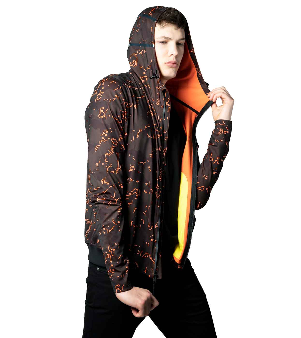 A model wearing the ELECTRIC ORANGE HOODIE from Machina - Wearable Technology poses against a white background, highlighting innovative fashion tech. This black hoodie, with striking orange patterns and lining visible in the hood and front, features waterproof zippers. The ensemble is finished with sleek black pants for a complete look.