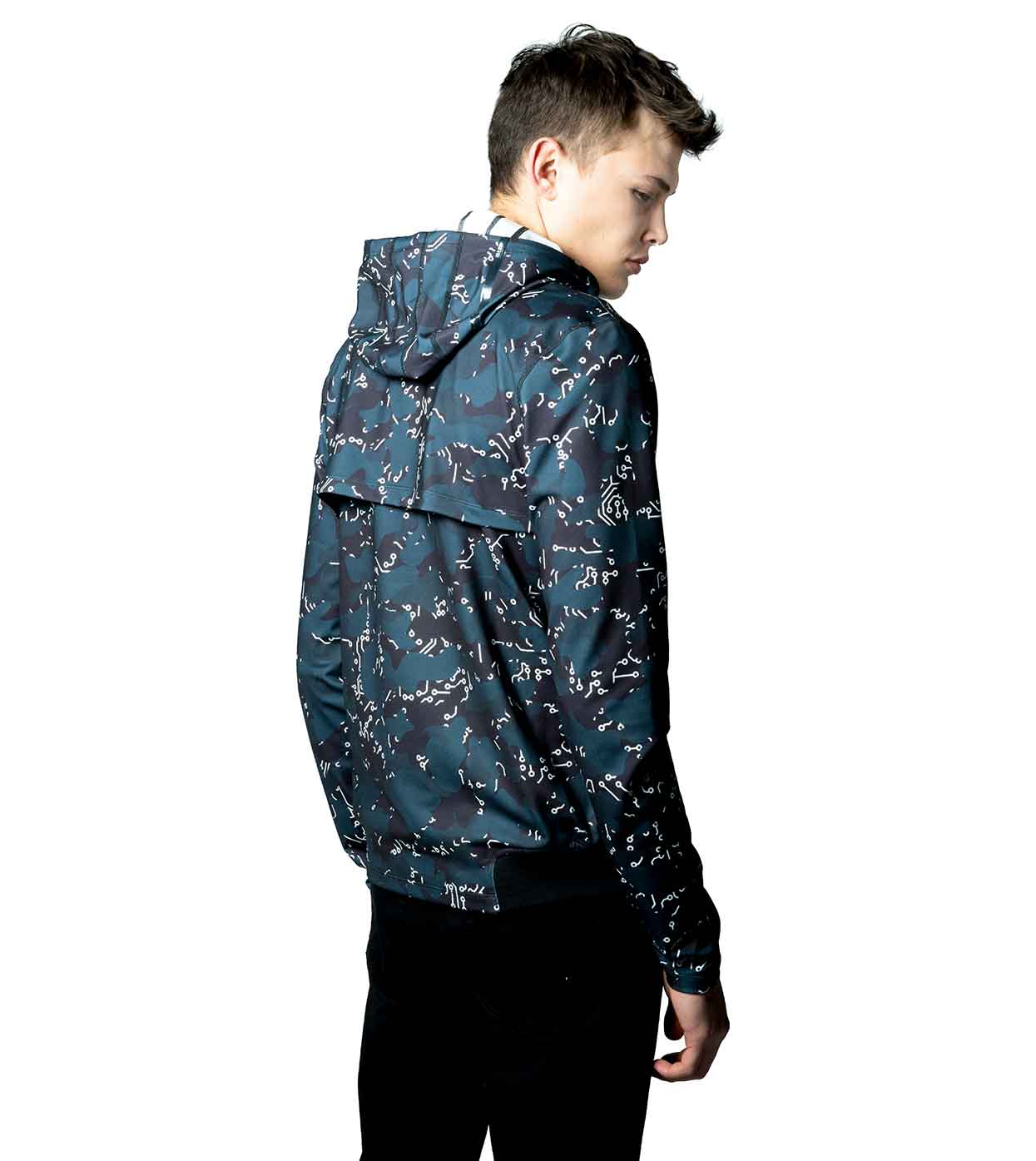 A person is seen standing sideways, looking to the right while wearing the ELECTRIC WHITE HOODIE from Machina - Wearable Technology. This advanced hoodie, featuring a stylish white abstract pattern against a blue backdrop, has its hood down. They are paired with black pants against a plain white background.