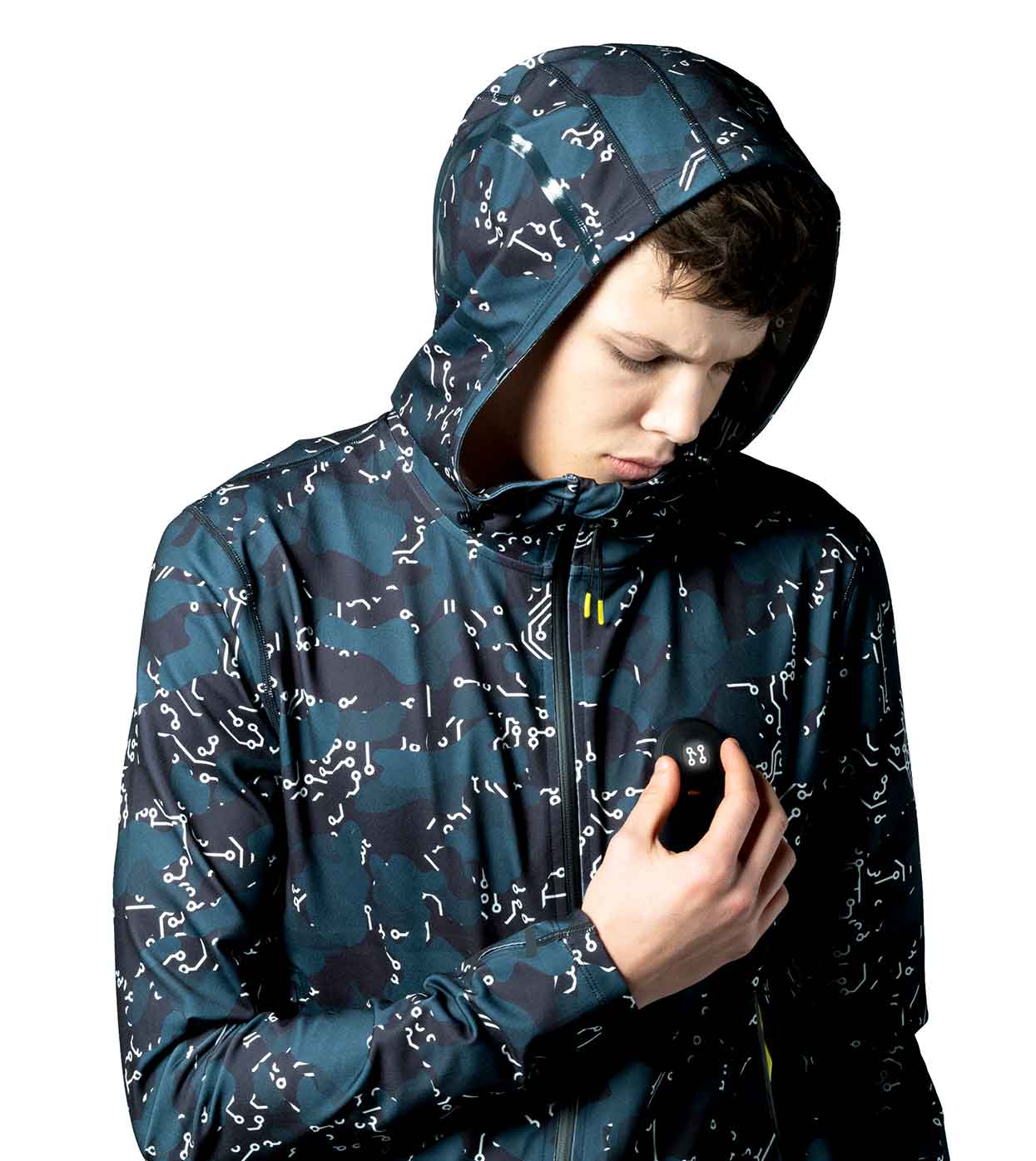 A person wearing the ELECTRIC WHITE HOODIE from Machina - Wearable Technology, featuring a dark camouflage and white abstract pattern, is looking down. This fashion tech piece has the individual gripping its edge near the chest against a plain white background.