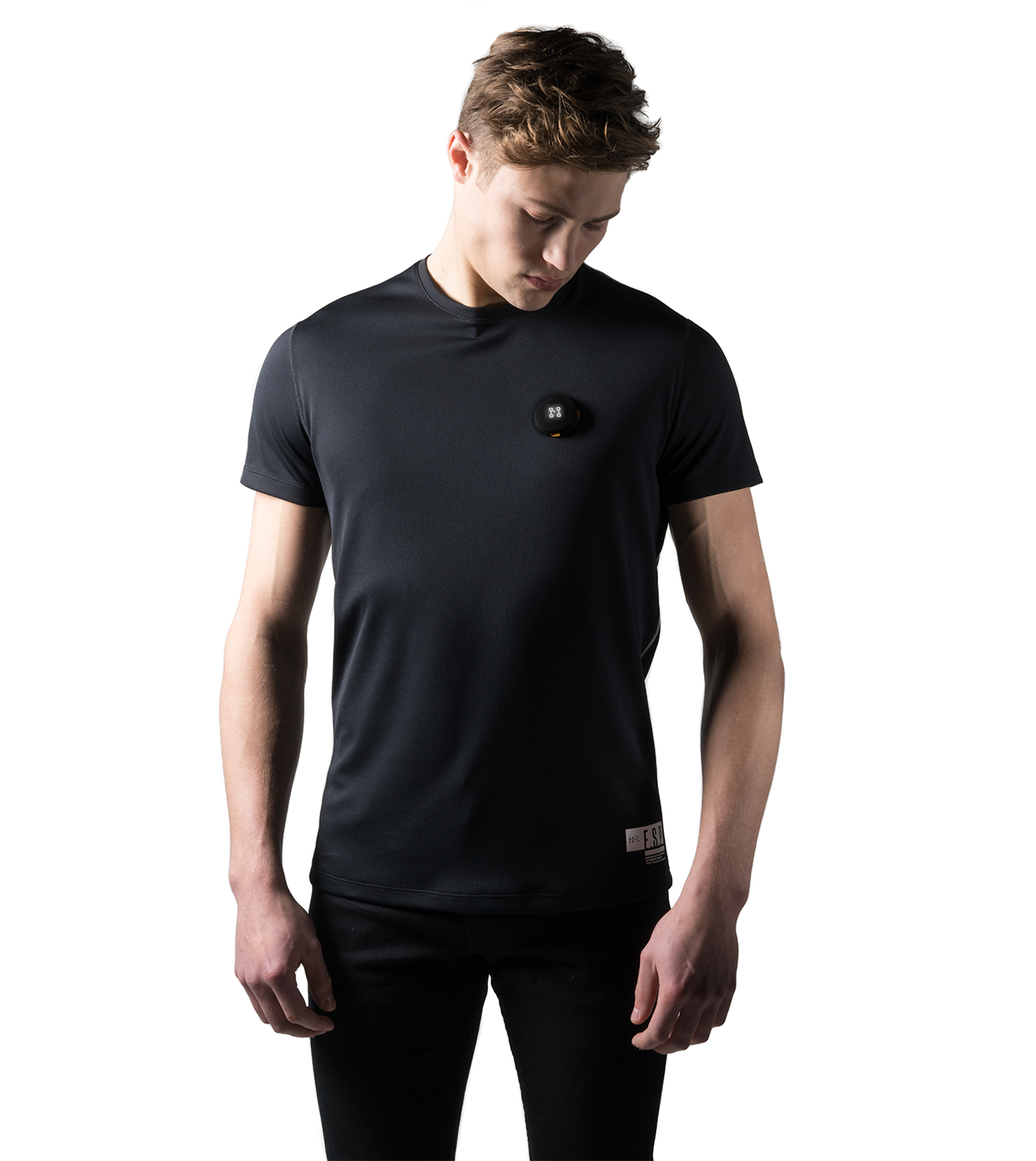 A person wearing the Smart Black T-shirt by Machina - Wearable Technology, crafted from recycled polyester, stands against a white background. The individual gazes downward with their hands at their sides. This sustainable fabric piece features a small round detail on the chest, blending style with eco-friendly choices.