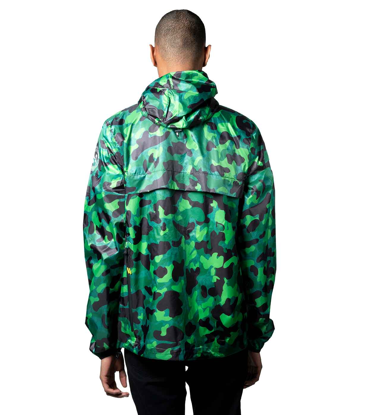 Wearing the AQUA-CAMO WINDBREAKER from Machina - Wearable Technology, a person stands with their hood up, showcasing its striking green camouflage pattern. Various shades of green and black form an eye-catching design. Paired with black pants against a plain white background, this ensemble exemplifies contemporary fashion technology.