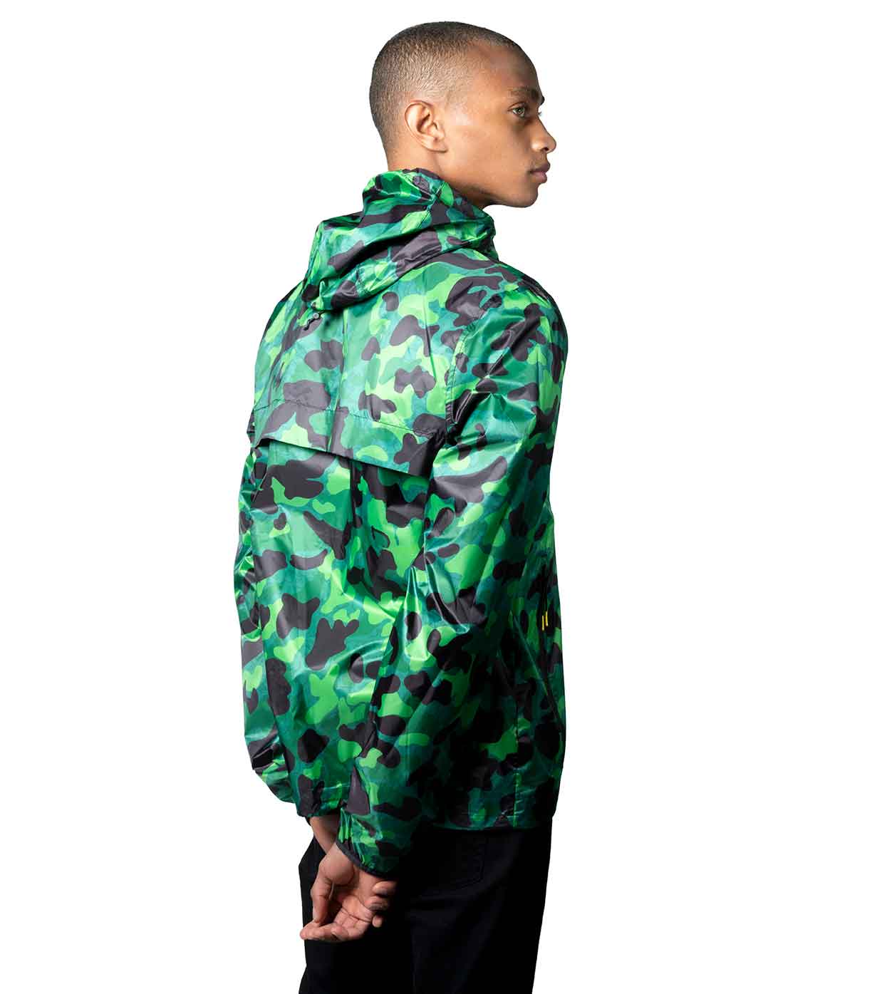 A person is observed from the side wearing the AQUA-CAMO WINDBREAKER by Machina - Wearable Technology paired with black pants, highlighting the fusion of style and fashion technology against a stark white background.