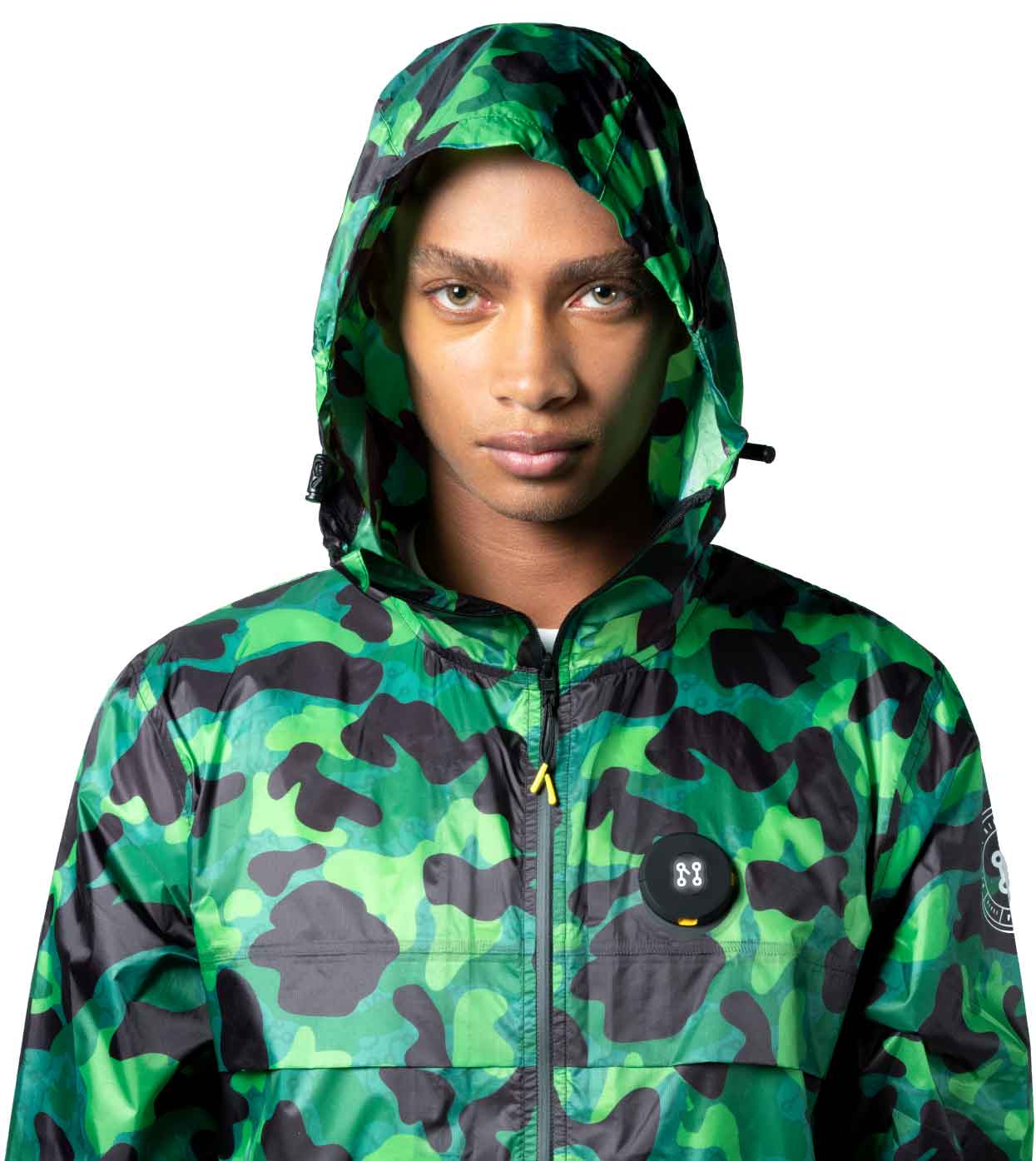 A person is seen wearing the Machina - Wearable Technology AQUA-CAMO WINDBREAKER, which comes in a green and black aqua camouflage design, against a white background. This innovative jacket features a round black emblem on the chest, effortlessly merging fashion and technology with style.