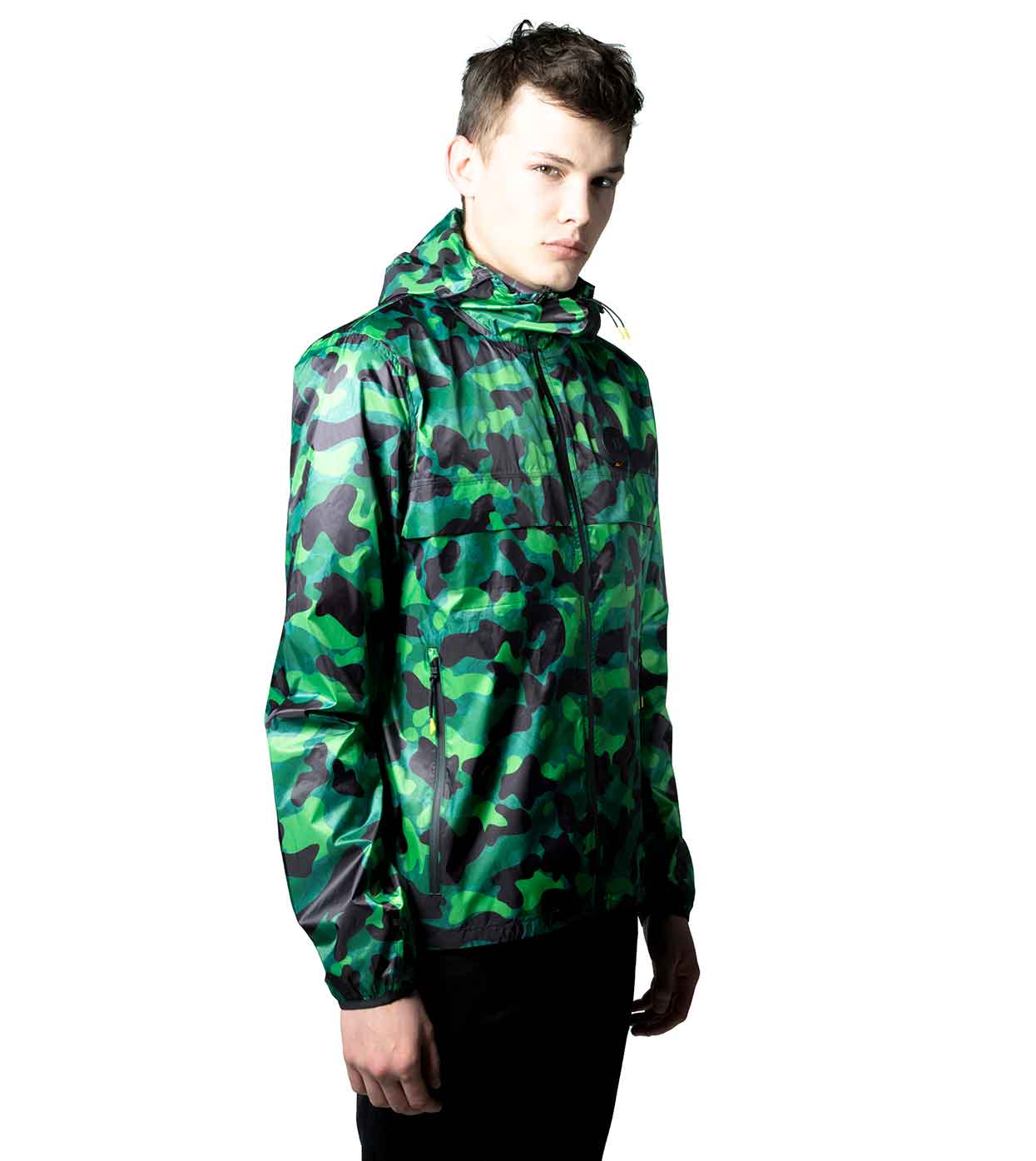 A person stands against a white background, looking to the side, wearing the GREEN-CAMO WINDBREAKER by Machina - Wearable Technology that cleverly blends fashion technology and style.