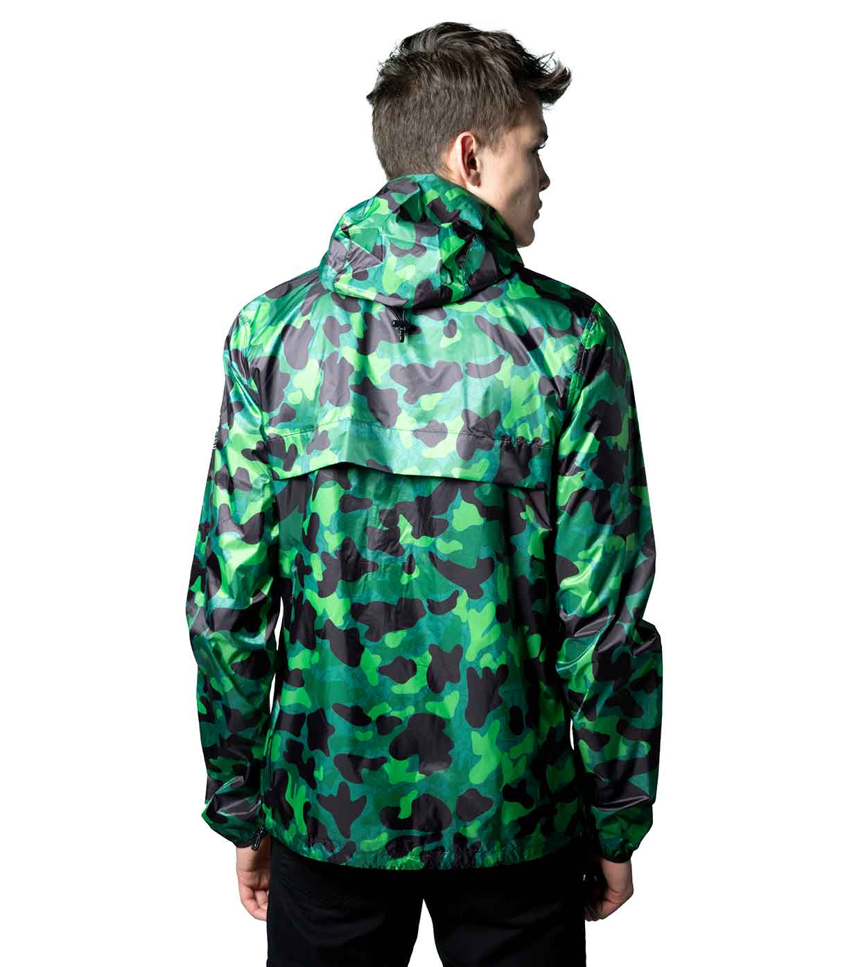 A person is seen from behind wearing the GREEN-CAMO WINDBREAKER by Machina - Wearable Technology, showcasing different shades of green and black in its smart design. The ultralight nylon jacket's hood is pulled up, and the individual, with short dark hair, pairs it stylishly with sleek black pants.
