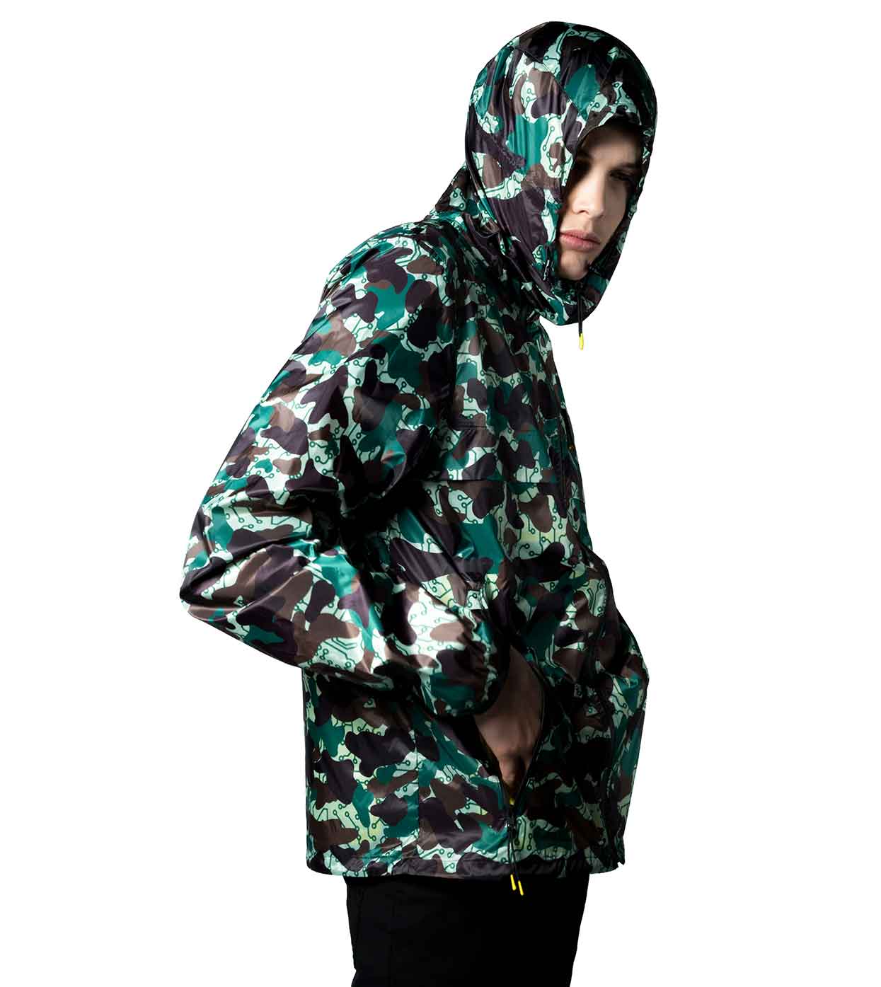 A person wears the JARHEAD CAMO WINDBREAKER by Machina - Wearable Technology, with their hands in the pockets, looking to the side against a plain white background.