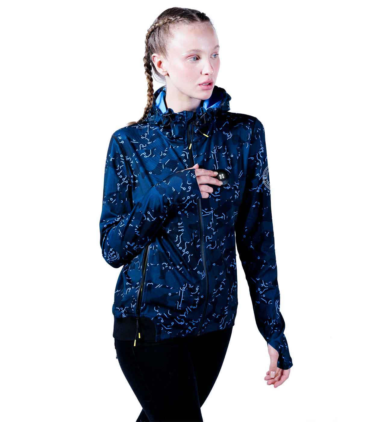 A person wearing the ELECTRIC BLUE HOODIE from Machina - Wearable Technology, designed with a constellation pattern and zippered pockets, is standing and looking to the side. Paired with black pants and braided hair, they embody the ultimate fusion of fashion tech and style.
