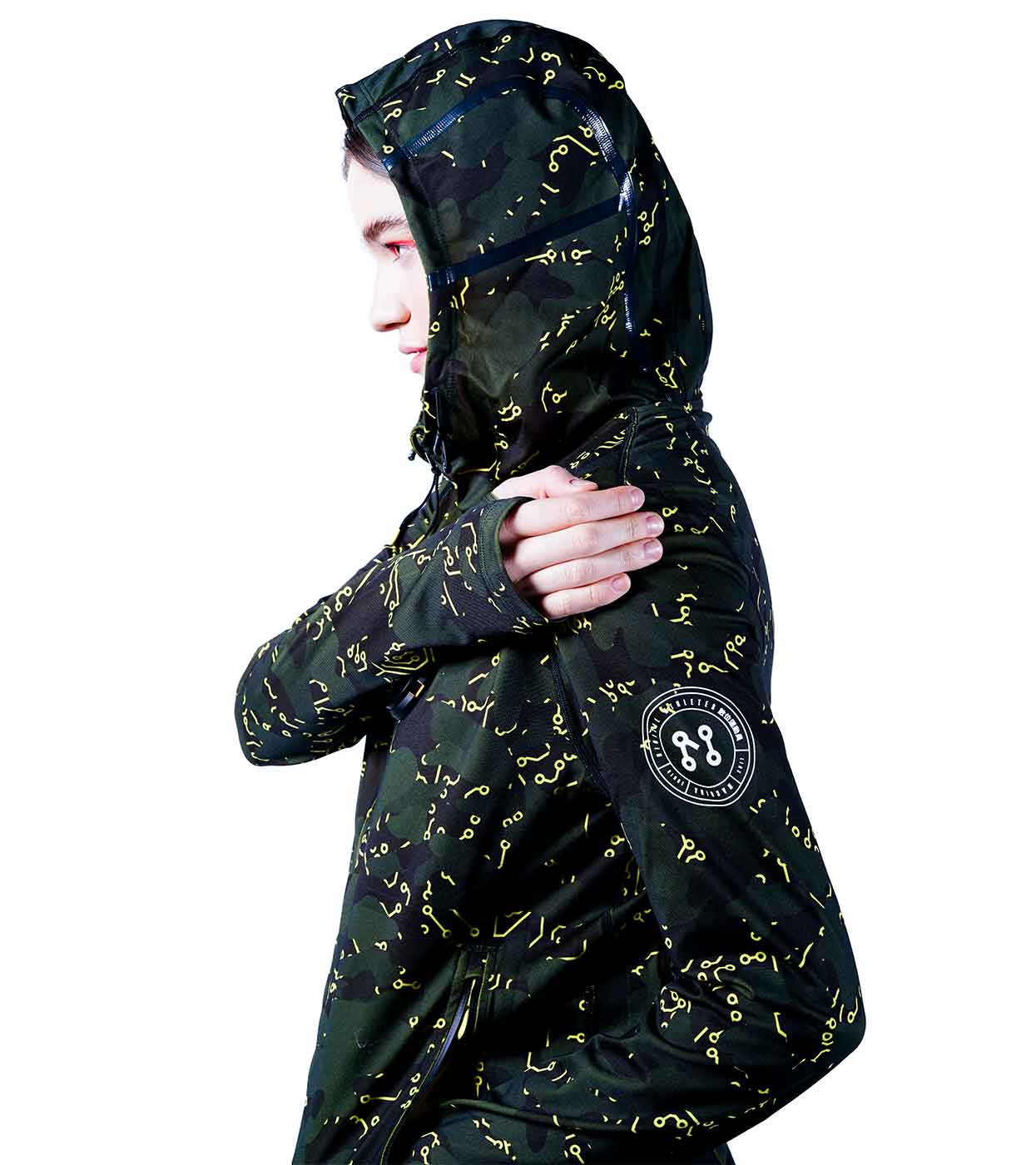 A person is shown wearing the ELECTRIC YELLOW HOODIE from Machina - Wearable Technology, which boasts an advanced design with a dark camo pattern accented by striking yellow elements. The individual is positioned sideways, adjusting the hood. The hoodie also features a black patch adorned with white symbols on the sleeve. With its sleek fashion tech elements, this eye-catching piece stands out against the white background.