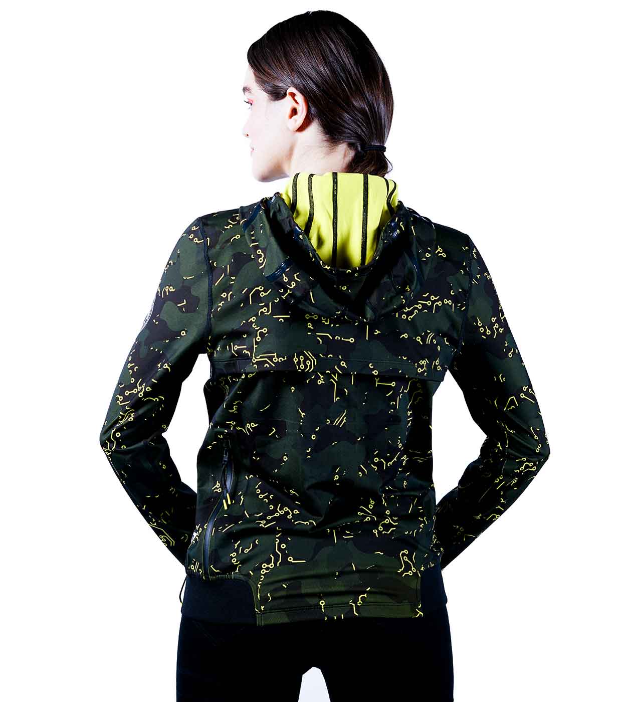 A person with long hair is facing away, donning the ELECTRIC YELLOW HOODIE by Machina - Wearable Technology. This smart hoodie, in green and black, features striking yellow patterns and boasts a hood lined with vibrant yellow fabric, highlighting fashion tech innovation. The setting is a plain white backdrop.